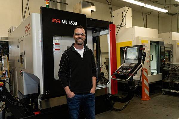 Shop Owner Evan Jones standing in front of his Methods Machining Center MB 450U